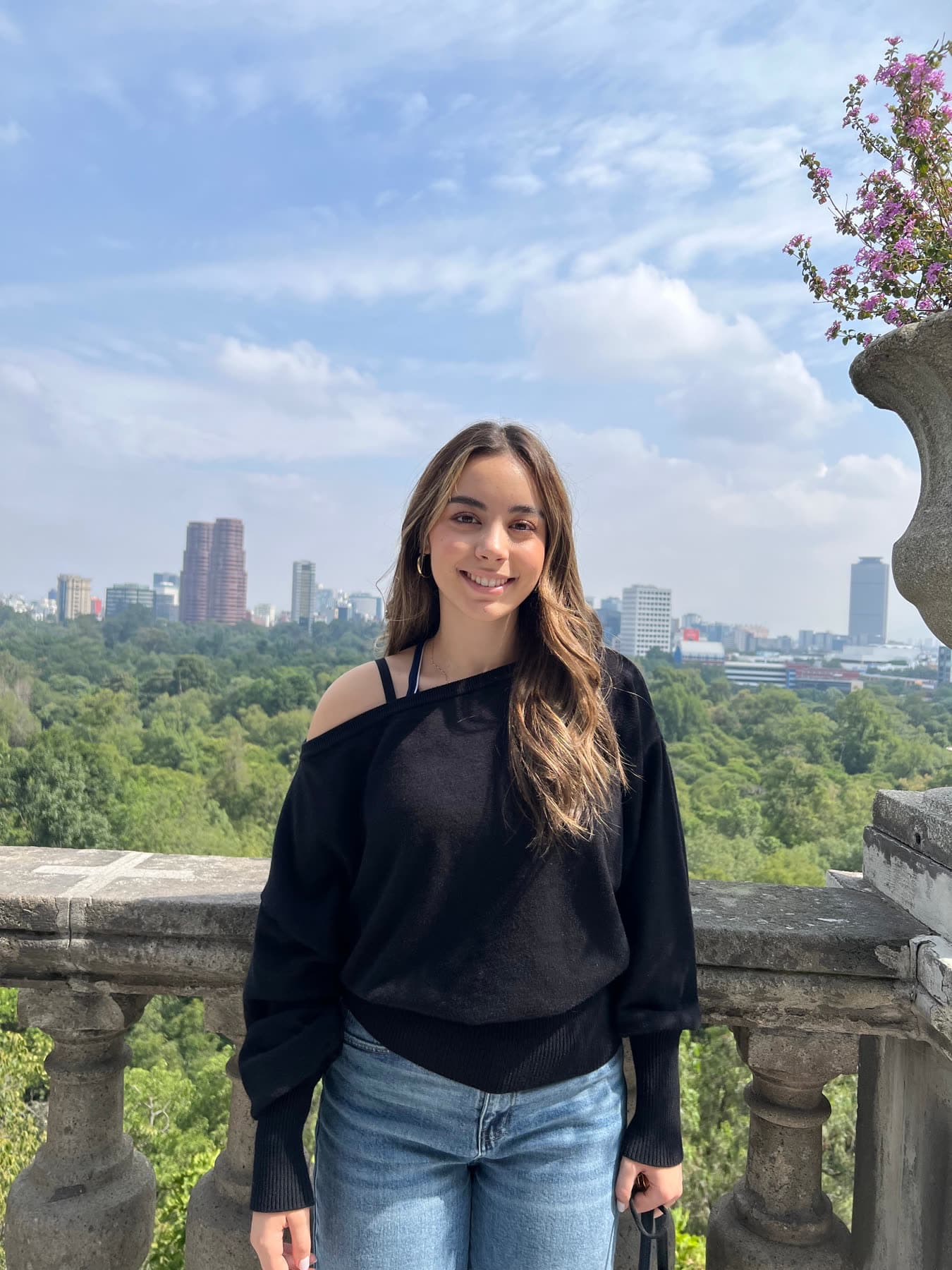 Ana Sofía Tamez al aire libre, sobre una terraza de piedra, con el bosque y los edificios de la ciudad detrás